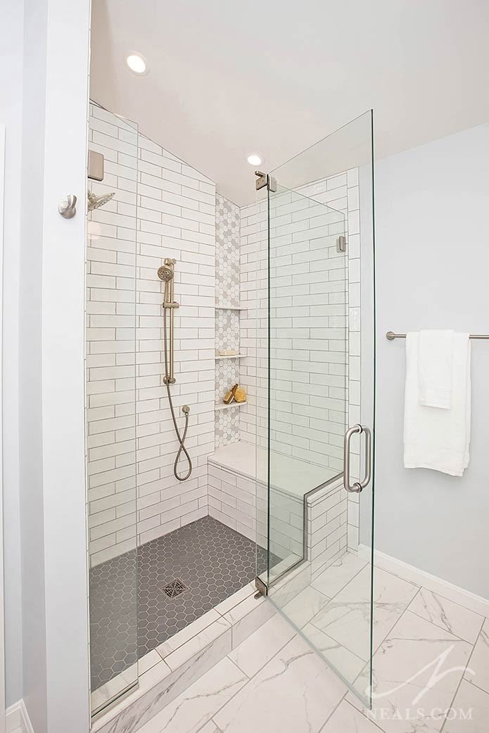 a walk in shower sitting next to a white tiled wall and floor with glass doors