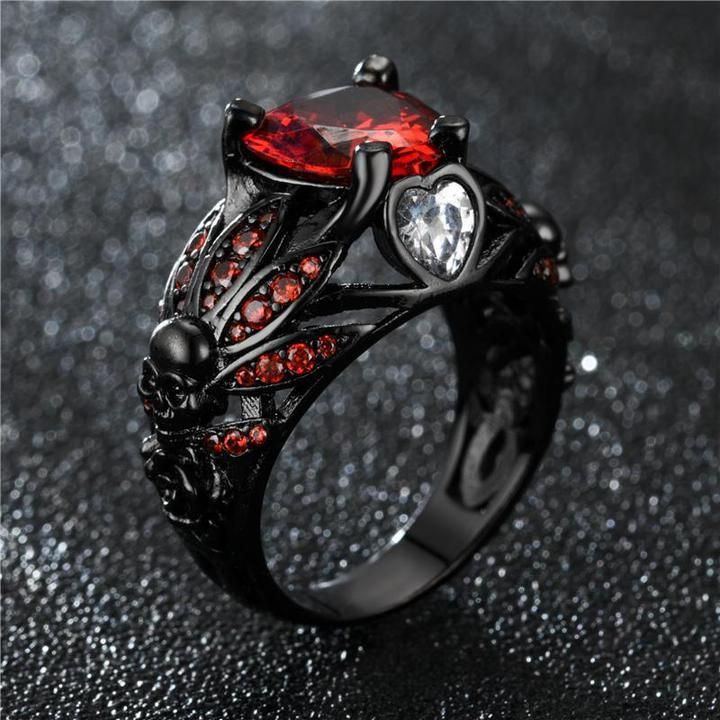 a black ring with red and white stones in the center on a glittery surface