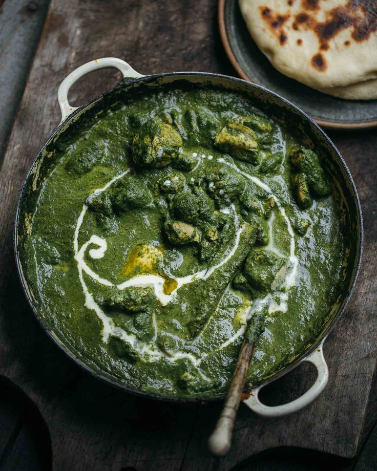 a pan filled with spinach and sauce on top of a wooden table next to pita bread