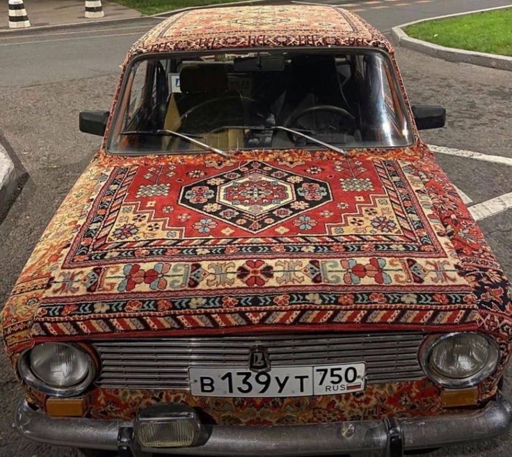 an old car is covered in colorful rugs