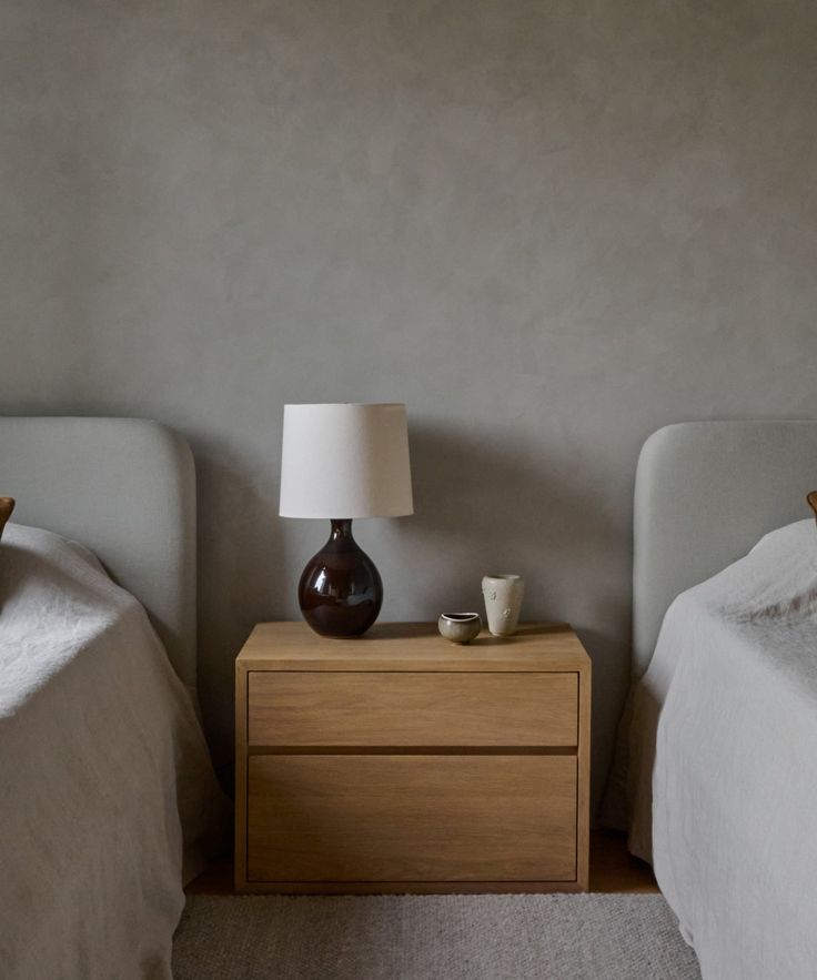 two beds with white linens and one has a brown vase on the night stand