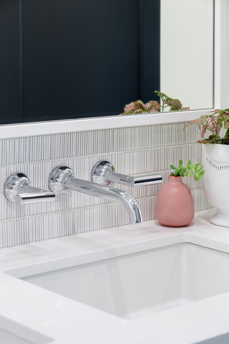 a white sink sitting under a bathroom mirror next to a potted plant on top of a counter