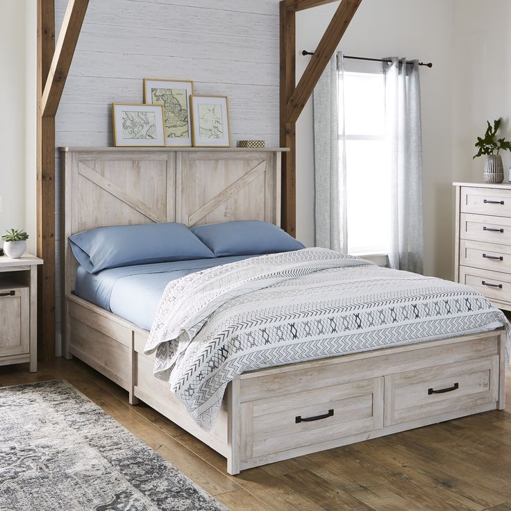 a white bed with blue sheets and pillows in a room next to a rug on the floor