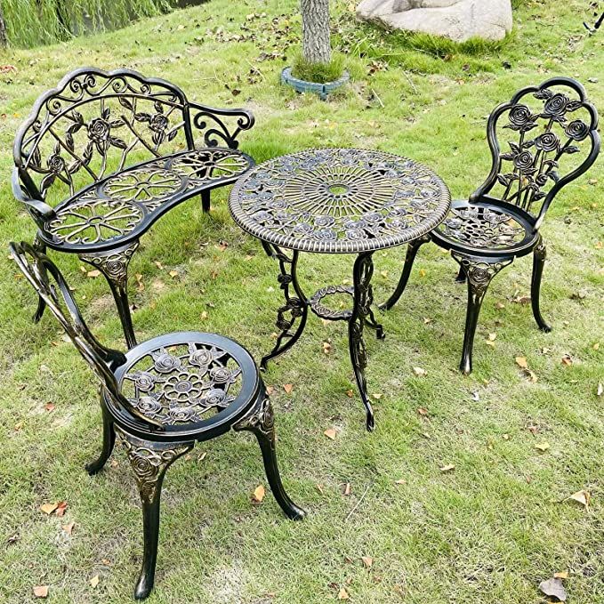 three wrought iron garden furniture sitting on the grass in a park, with one table and two chairs