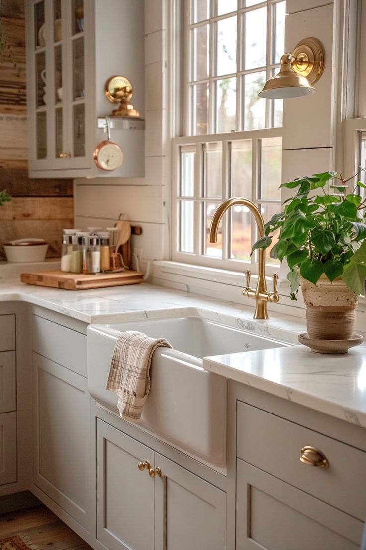 a kitchen with white cabinets and gold hardware on the doors, windows, and sink