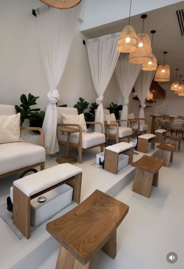 a room filled with white couches and wooden tables next to hanging lights above them