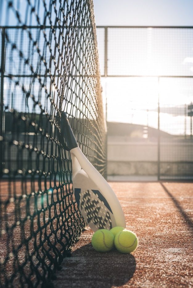 two tennis balls and a racket are on the ground next to a fence with chain link fencing