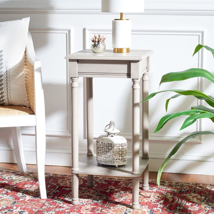 a small table with a lamp on it next to a white chair and potted plant