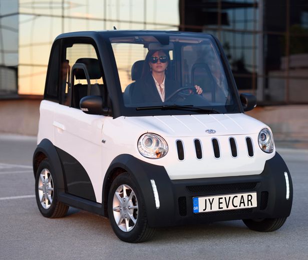 a woman driving a small white car in front of a building