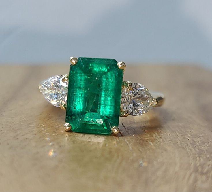 This stunning 14k yellow engagement ring features a beautiful 4.37ct natural green emerald in a rectangular shape. The ring is adorned with two diamonds and one gemstone, and the main stone is treated with oiling . The ring is size 6 and can be resized if needed.  Gorgeous 14K Yellow Gold Engagement natural green emerald Ring.  center natural emerald weight 4.37ct. size 11x7.7mm very nice rich vivid green color, nice luster, very lively, nice cut, clean emerald.brilliant, sparkly emerald.  side two pear lab-grown diamonds total weight of 1.38ct. Size 7.6x4.9mm G-VS1 White, bright stone, sparkly lively brilliant diamonds. ring size 6 Resizable  Appraisal available  Retail value $14,500 net. The cocktail style ring is perfect for engagement or anniversary occasions, and the three-stone setti Luxury Gold Emerald-cut Birthstone Ring, Luxury Yellow Gold Emerald Ring With Center Stone, Luxury Emerald Ring With Intricate Design, Luxury Yellow Gold Emerald Ring With Gemstone Accents, Luxury Open Ring With Emerald, Luxury Gold Emerald Ring With Exquisite Style, Luxury Green Diamond Ring With Diamond Cut, Yellow Engagement Ring, Green Emerald Ring