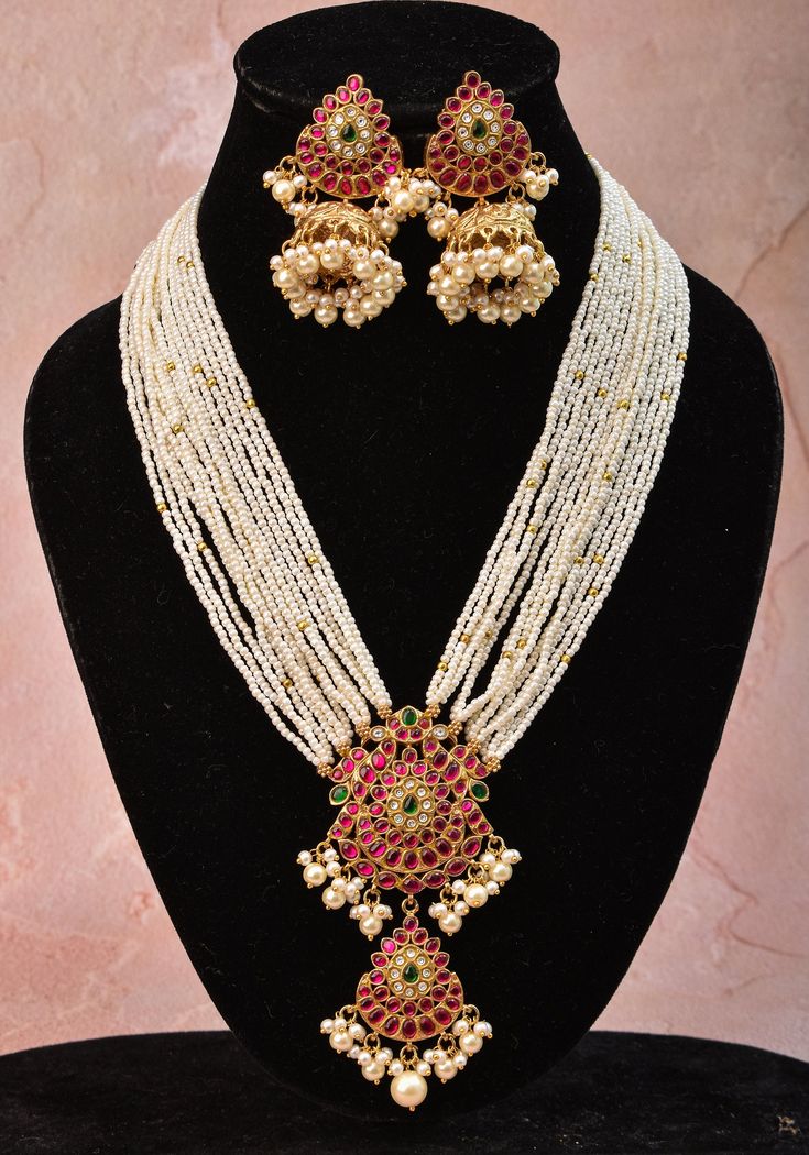 Looking for something aesthetic and Royal? Your search ends with is Multistrand bead choker in shades of white and green. A prominent central unit features the jaadu stones in twin peacock designs and hanging beads balance it with timeless beauty.  This statement piece undoubtedly sits beautifully on your neck! The adjustable closure makes it convenient to wear as well.  The set includes a matching pair of earrings that works graciously with the choker and also by itself.  Note: This jewelry has Traditional White Kundan Necklace With Gemstone, White Gemstone Jewelry For Festivals, Traditional White Bridal Necklace With Gemstone, White Kundan Necklace With Gemstone, White Temple Jewelry Necklace With Gemstone, Traditional White Pearl Necklace With Gemstone, White Gemstone Temple Jewelry Necklace, Handmade White Kundan Beaded Necklaces, Handmade White Kundan Beaded Necklace