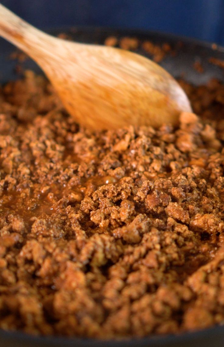 a wooden spoon stirring some food in a skillet with brown sauce on it and another item to the side