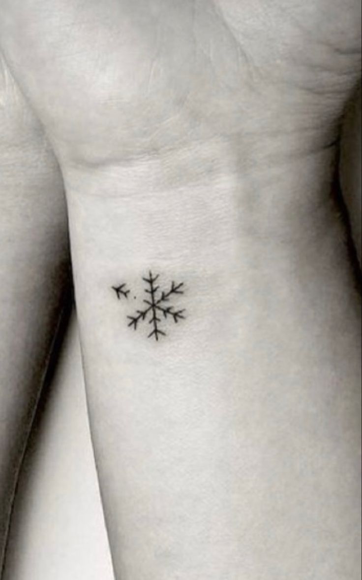 a small snowflake tattoo on the left side of the arm, with three birds flying around it