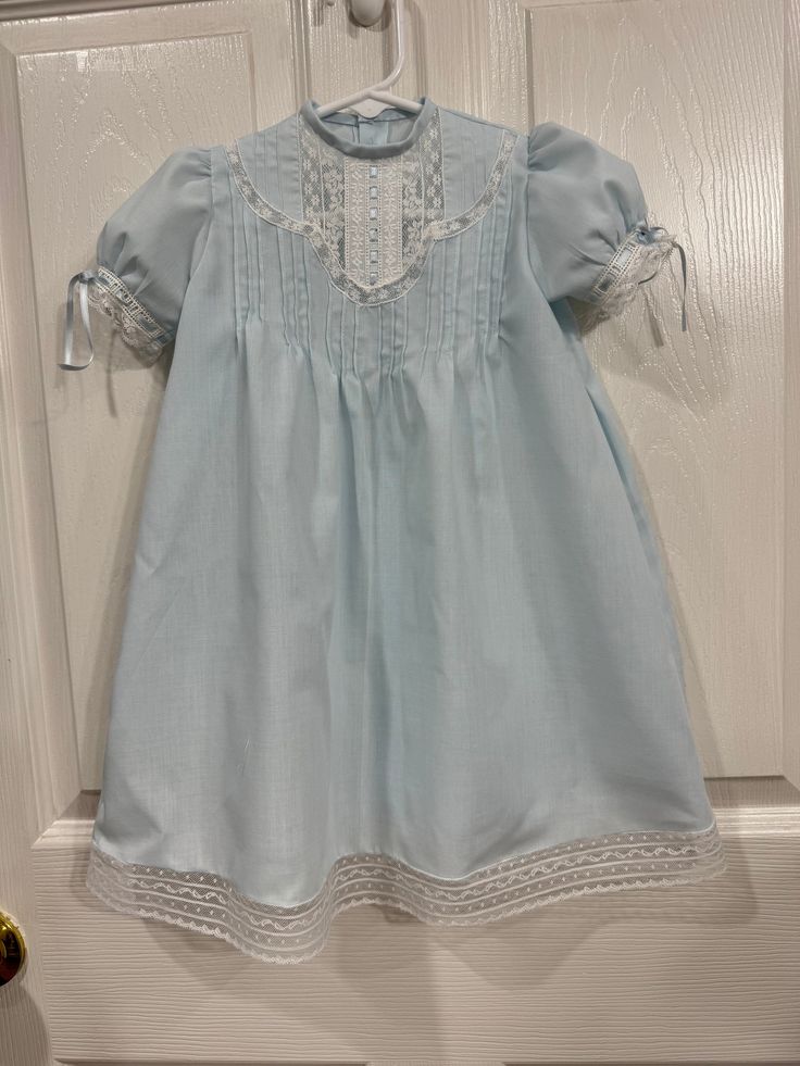 This is a newborn to 3 month blue batiste baby heirloom daygown with white lace. The dress buttons down the back.   There is lace on the bottom of the sleeve with blue silk satin ribbon running through it. There is a lace band around the bottom of the skirt with lace edging. The length is 20 1/2 inches. Elegant Fitted Blue Baptism Dress, Blue Dresses With Lace Collar For Daywear, Blue Vintage Victorian Dress With Lace Trim, Vintage Blue Victorian Dress With Lace Trim, Blue Victorian Dress With Lace Trim, Blue Lace Trim Dress For Baptism, Fitted Baptism Dress With Lace Trim For Daywear, Fitted Baptism Dress With Lace Trim, Baby Heirloom