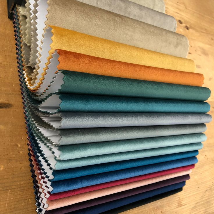 a stack of different colored fabrics sitting on top of a wooden table next to each other