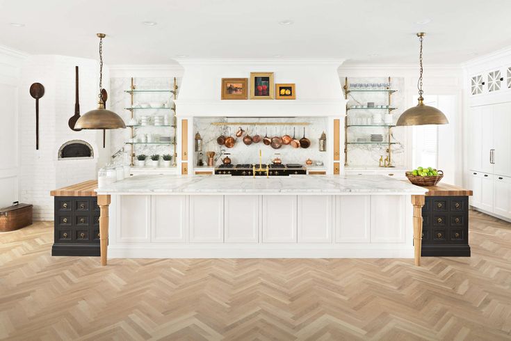 a kitchen with white cabinets and wood flooring is pictured in this image, there are two hanging lights above the island