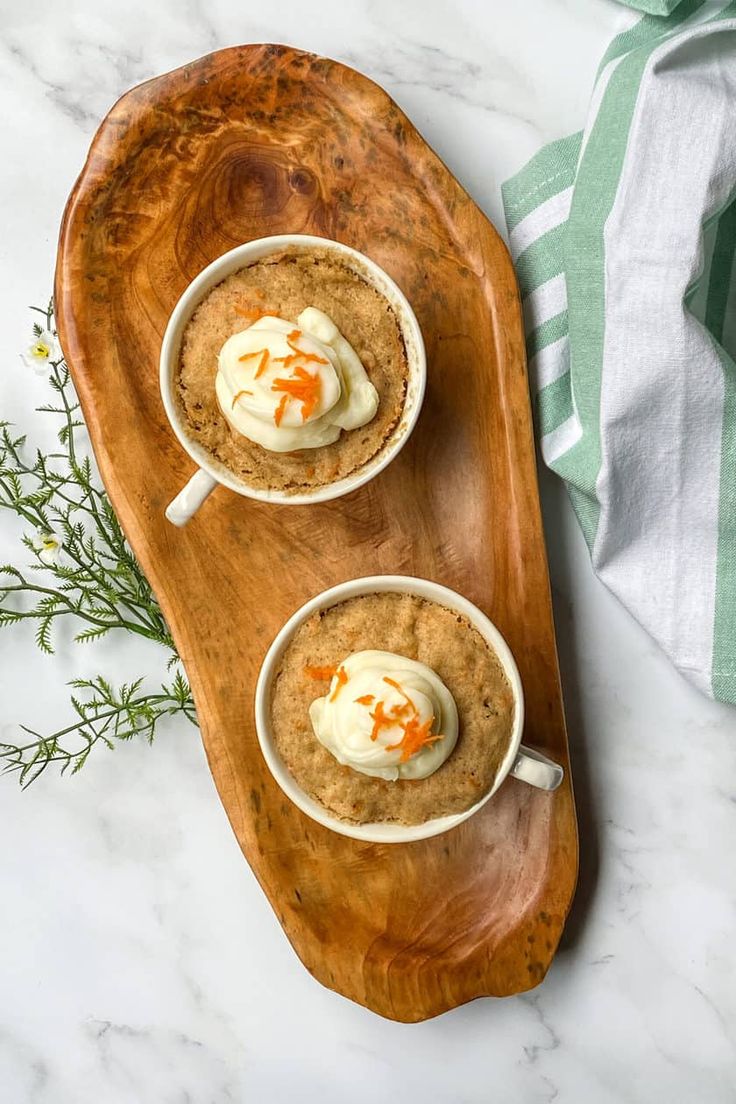 two cups filled with oatmeal and topped with whipped cream on a wooden platter