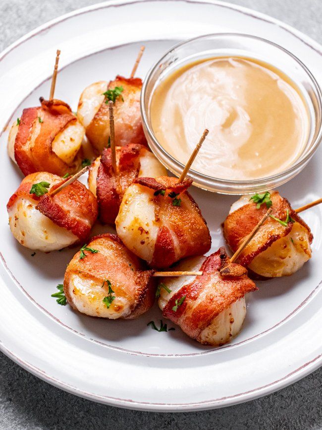 bacon wrapped scallops and dip on a white plate with a bowl of dipping sauce