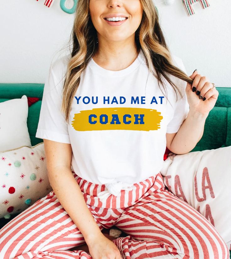 This "You Had Me At Coach" design is the perfect, fun Ted Lasso shirt for anyone that loves sports and Ted Lasso! Athleisure Graphic Print T-shirt For Game Day, Crew Neck T-shirt With Sublimation Print For Cheerleading, Sports Fan Apparel Tops With Sublimation Print, Fan Apparel Sports Tops With Sublimation Print, Team-colored Crew Neck T-shirt For Cheerleading, Sports Slogan T-shirt Crew Neck, Crew Neck Slogan T-shirt For Sports, Sporty Team Name T-shirt For Workout, White Graphic Tee With Sublimation Design For Sports