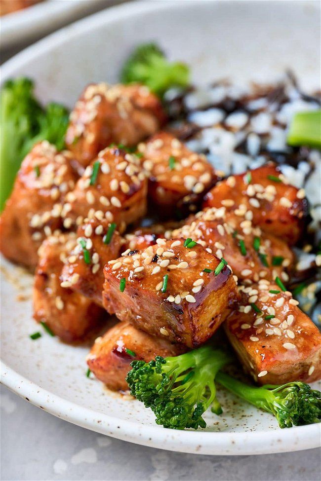 a white plate topped with meat and broccoli covered in sesame seed flakes