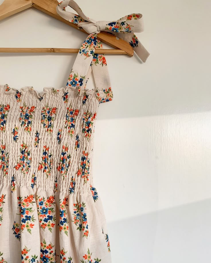 a dress hanging on a wooden hanger in front of a white wall with flowers