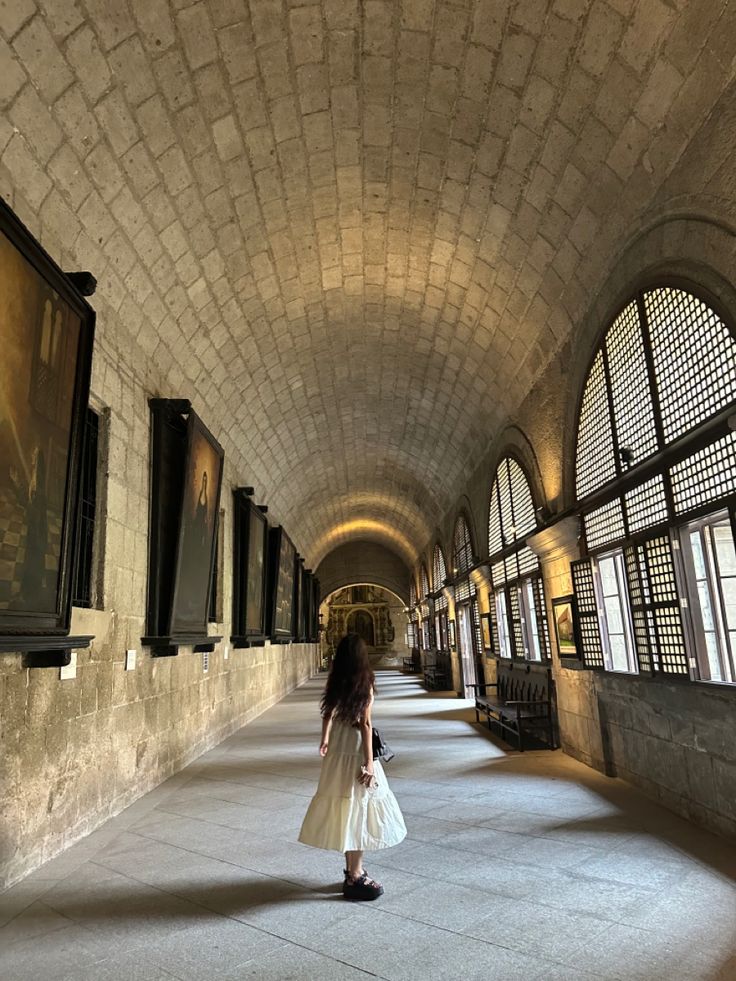 a long hallway with arched windows and benches on the side walk in an old building