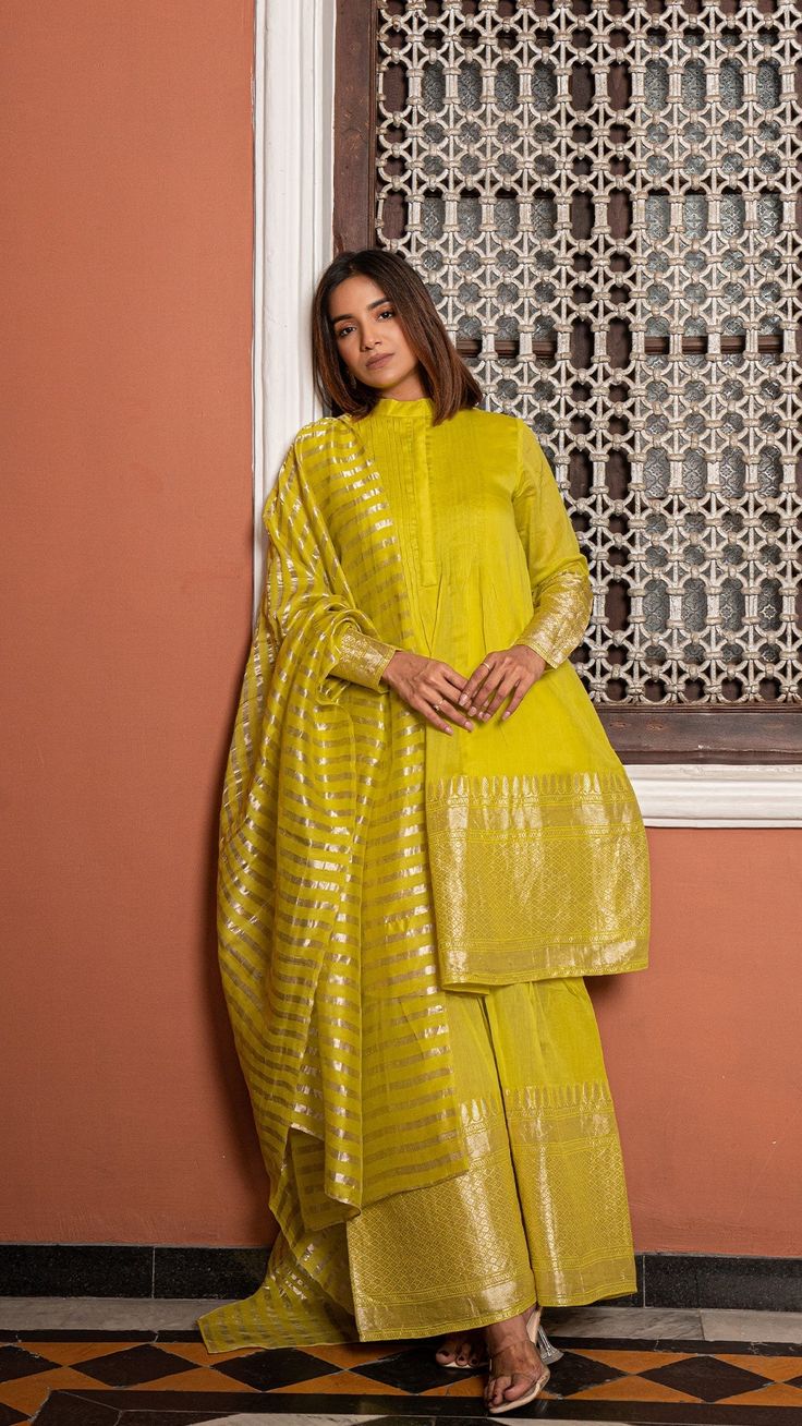 Bring on the festive spirit with our kurta set in pure woven chanderi silk.nFully lined kurta with sharara pants.nKurta and Sharara Fabric : Pure Woven Chanderi Silk.nDupatta : Pure Tissue.nColour : Lime Green.nModel height is 5.4” and is wearing a size S.nWash Care : Dry Clean Only.nThis product will be exclusively handcrafted for you, making the colour/texture/pattern slightly vary from the image shown, due to multiple artisan-led techniques and processes involved. Chanderi Kurta Designs Latest, Chanderi Silk Salwar Suit Designs, Pattu Sharara Designs, Tissue Silk Dress Designs, Tissue Kurta Set, Eid Chanderi Palazzo Set With Gota Work, Chanderi Palazzo Set With Resham Embroidery For Diwali, Navratri Chanderi Palazzo Set With Zari Work, Chanderi Palazzo Set With Traditional Drape For Diwali