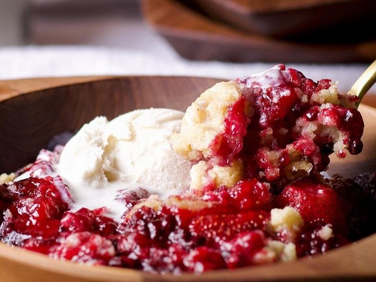 a wooden bowl filled with ice cream and cranberry cobbler topping on top of it