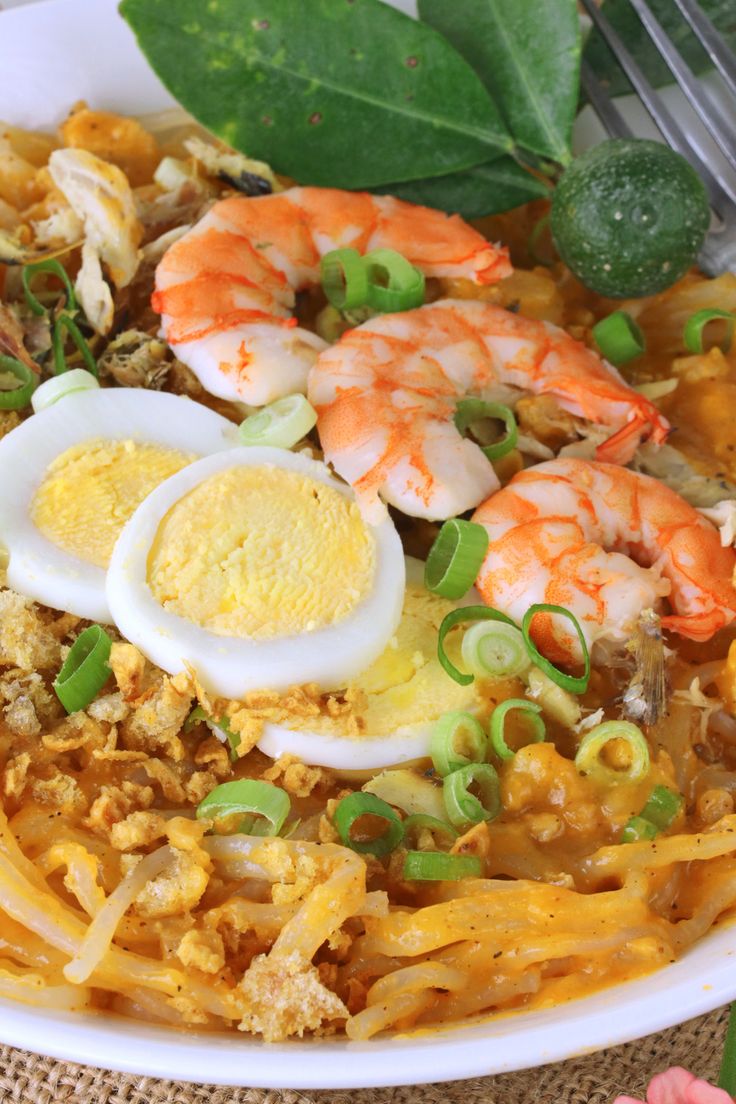 a white bowl filled with noodles and shrimp next to a fork on top of a table