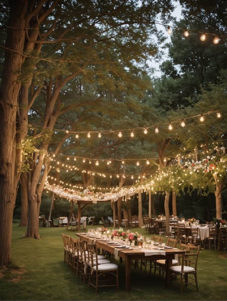 an outdoor dining area with string lights strung over the tables and chairs, surrounded by trees