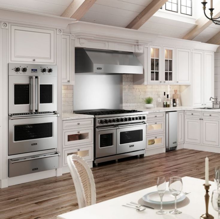 a large kitchen with white cabinets and stainless steel stove top ovens, dining room table and chairs