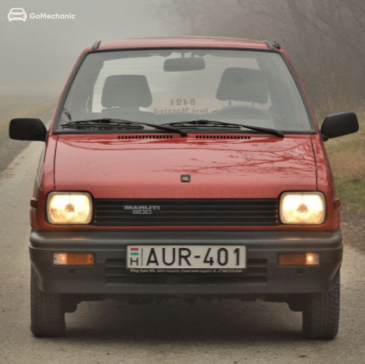 a red car driving down a road next to grass and trees on a foggy day