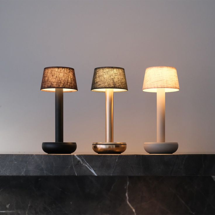 three lamps sitting on top of a table next to each other in front of a wall