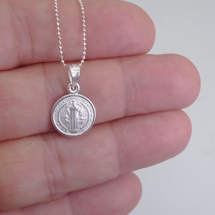 St. Benedict full-body image and a cross in the back Material that is extremely durable and hypoallergenic A powerful message of spiritual protection The front and back of this pendant are finely detailed, and the chain that it hangs from is no exception. The delicate details are embossed in a silver tone for better shine and shadowing for better contrast. This double-sided necklace is a must-have accessory. Pair this with any other necklace for a stylish and modern look. Dimensions & Specificat Sterling Silver Medallion For Blessing Occasion, Sterling Silver Charm Necklace With Coin Pendant, Sterling Silver Charm Necklace With Oval Coin Pendant, Sterling Silver Charm Necklaces With Coin Pendant, Adjustable Sterling Silver Coin Pendant Jewelry, Adjustable Sterling Silver Coin Pendant, Symbolic Sterling Silver Pendant Medallion Necklace, Sterling Silver Spiritual Coin Pendant Jewelry, Spiritual Sterling Silver Coin Pendant Jewelry