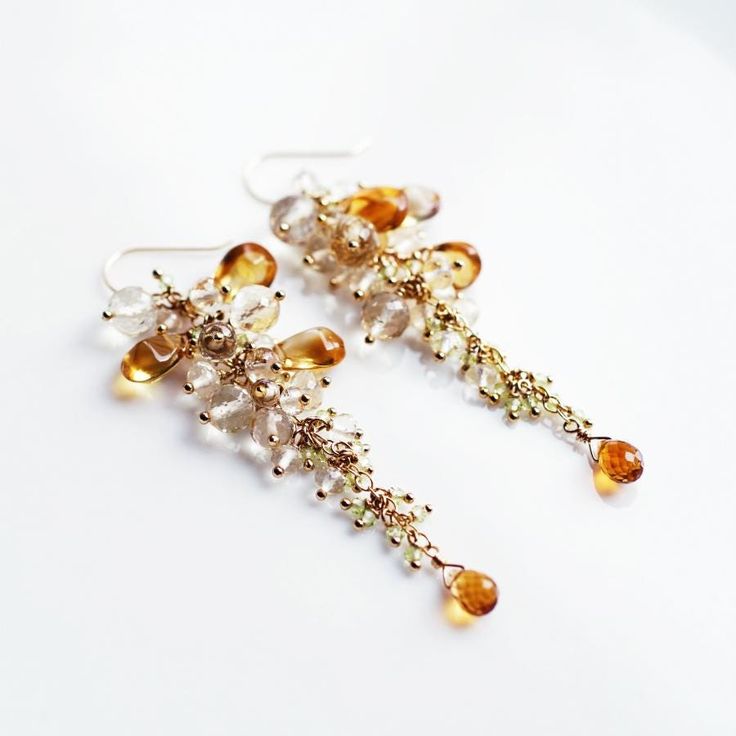 Citrine, Scapolite, and Peridot Chandelier Earrings - Yellow Wisteria Golden chain 【 Wisteria 】 We have fashioned a pair of jewelry using yellow wisteria, whose flowers gently sway overhead. It took about half a day to carefully select the stones, then pin them together while checking the balance, creating a three-dimensional reproduction with real wisteria flowers in front of us. It is impossible to convey in a photograph the way it sways gracefully as it hangs, the way it reflects a delicate glow, and the soft feeling it gives as it rests against your profile. This is a special piece of jewelry with an emotional expression that only the real thing can have. The rare plain pear-shaped citrine has a moist glow when it shines through the sunlight, the finest cut scapolite has a fleeting and Yellow Wisteria, Wisteria Flowers, Emotional Expression, Soft Feeling, Golden Chain, November Birthstone, The Balance, Wisteria, Gorgeous Design