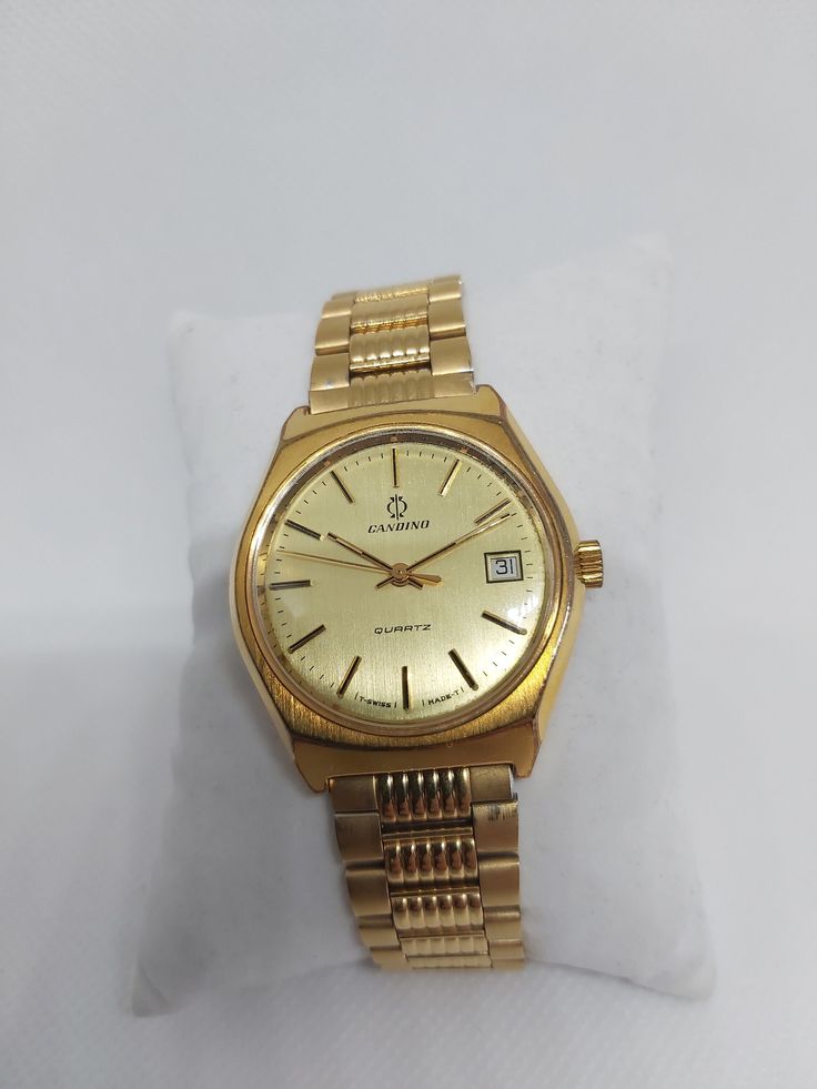 This vintage Candino Quartz men's watch exemplifies classic Swiss craftsmanship with its timeless design and reliable performance. Featuring a golden dial, gold-toned hands, and markers, this watch radiates elegance. The original gold-toned stainless steel bracelet and clasp enhance its sophisticated appearance. Candino is a reputable Swiss watch brand known for its dedication to quality and precision. Founded in 1947, Candino has built a strong reputation in the watchmaking industry by producin Vintage Gold Analog Watch, Gold Vintage Analog Watches, Retro Gold Watches With Subdials, Gold Retro Watches With Subdials, Retro Yellow Gold Watch With Chronometer, Retro Gold Analog Watch Accessories, Retro Yellow Gold Chronometer Watch, Vintage Gold Watches With Subdials, Vintage Gold Watch With Subdials