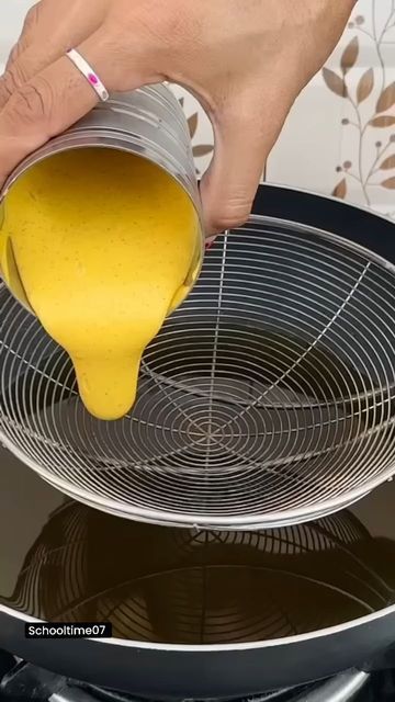 a person pouring yellow liquid into a pot on top of a black stovetop burner