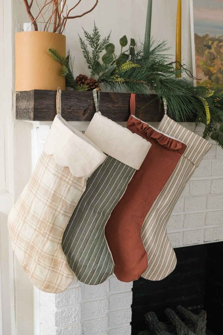 three stockings hanging from a mantel decorated with greenery