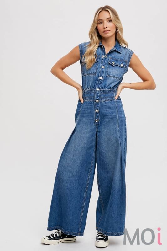 The denim sleeveless shirt jumpsuit is a stylish and versatile garment that combines the classic charm of denim with the ease and comfort of a jumpsuit. It features a sleeveless design with a button-down front, resembling a shirt, and a tailored bottom that flows into pants or shorts. This piece offers a casual yet trendy vibe, ideal for various occasions, from casual outings to relaxed gatherings. -Model is 5'9" and wearing a Small Sleeveless Denim Jumpsuit With Pockets, Casual Cotton Denim Jumpsuit With Buttons, Casual Wide-leg Jumpsuits And Rompers With Button Closure, Casual Wide Leg Jumpsuits And Rompers With Button Closure, Spring Overall Jumpsuit With Buttons, Spring Overall Jumpsuits And Rompers With Buttons, Medium Wash Sleeveless Denim Jumpsuit For Work, Denim Wide Leg Jumpsuits For Summer, Sleeveless Medium Wash Denim Jumpsuit For Work