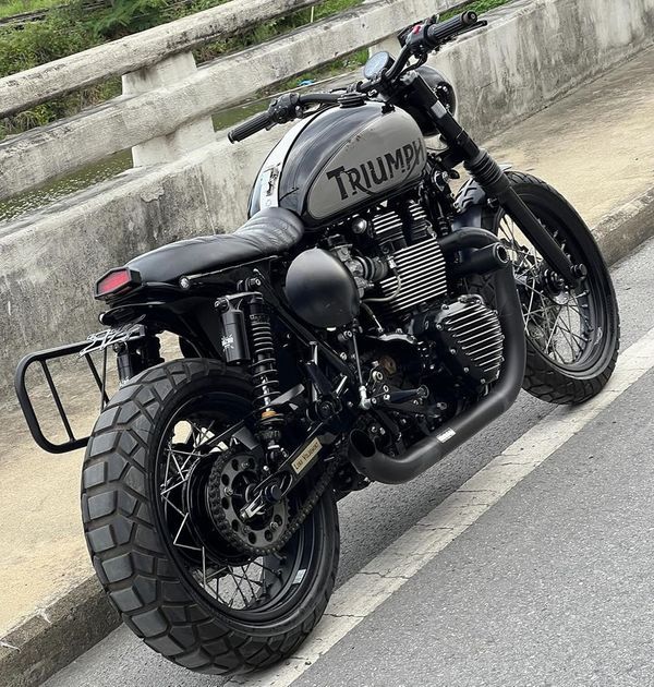 a black triumph motorcycle parked on the side of the road next to an overpass