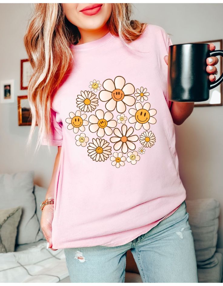 a woman is holding a coffee mug and wearing a pink shirt with flowers on it