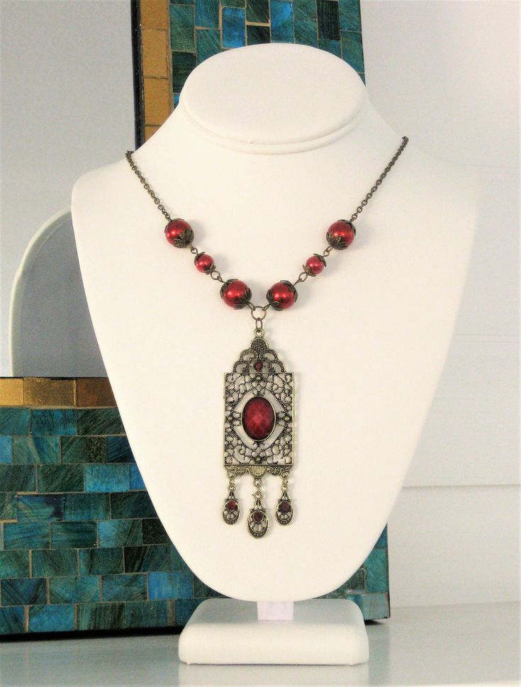 Red Victorian Style Necklace, handmade by Ralston Originals. This red pearl necklace is made with a large antique gold pendant, with red cabochon center, and 3 small charm dangles in antique gold with red crystals. The pendant is 3.5 inches long including the dangles, and 1 inch wide. The pendant is on antique gold brass chain, with dark red glass pearl beads, and antique gold bead caps. This Victorian red necklace is 18 inches long. This necklace is ready to send today, and it includes free shi Vintage Red Jewelry With Dangling Beads, Antique Red Beaded Necklaces For Gift, Antique Red Beaded Necklace For Gift, Vintage Red Beaded Necklace For Festive Occasions, Ornate Handmade Red Necklace, Antique Red Necklaces With Vintage Charm, Vintage Red Pendant Beaded Necklace, Vintage Red Necklace With Dangling Beads, Vintage Red Beaded Pendant Necklace