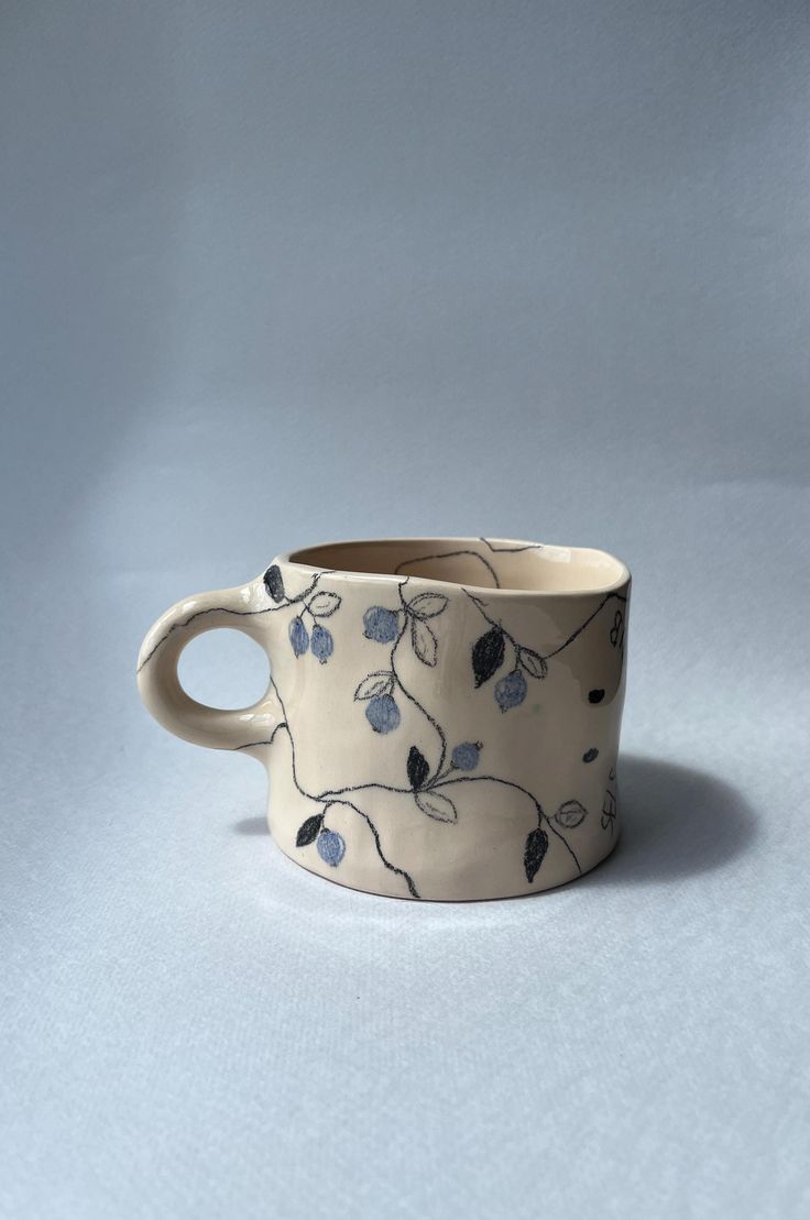 a white cup with blue flowers painted on the outside and inside, sitting on a gray surface