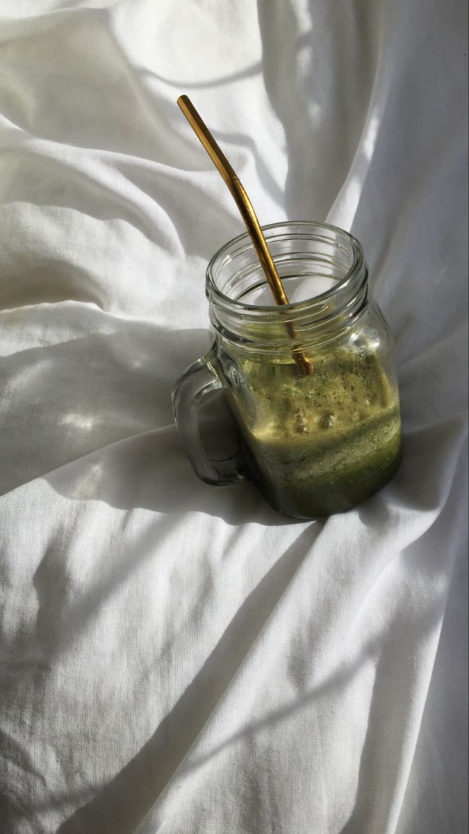 a jar filled with green liquid sitting on top of a white sheet