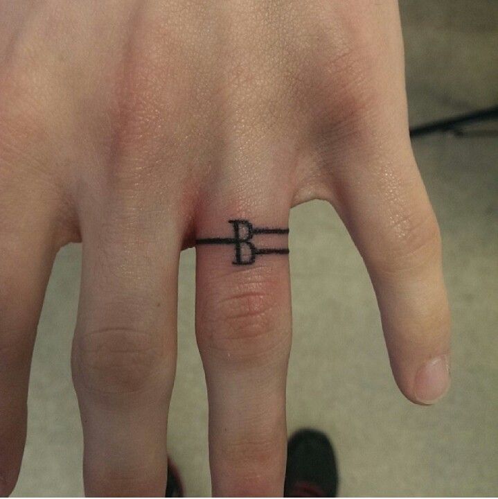 a person's hand with a small ring tattoo on the middle finger that has a letter b in it