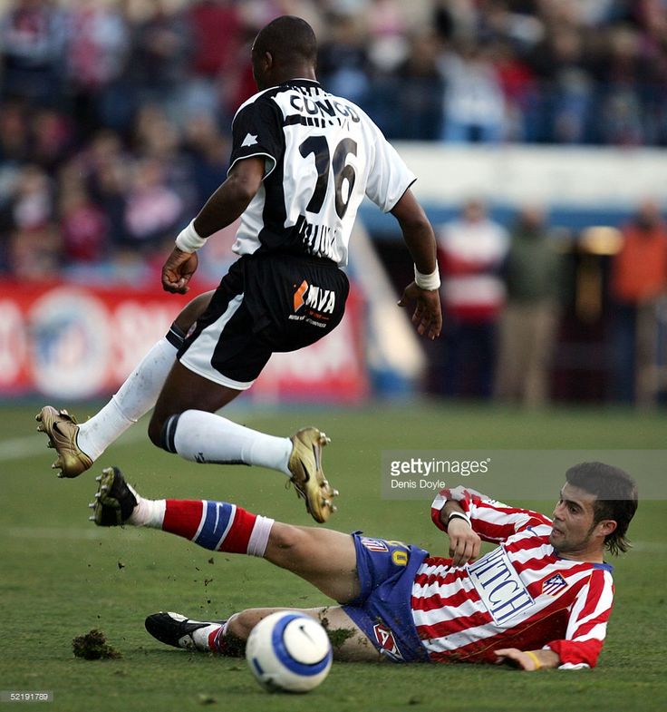 two men playing soccer on a field with fans in the stands watching from the stands