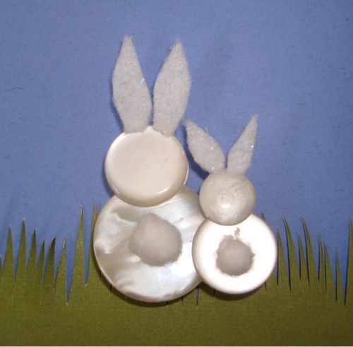 two white buttons with bunny ears on them sitting next to grass and blue sky in the background