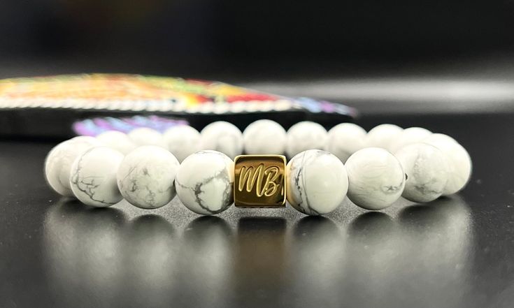 Discovered in Nova Scotia, "White Buffalo" stone has great calming properties. It will give you the gift of wisdom and enlightenment. Howlite's unique pourous texture feels great against the skin. Memory, Patience, Knowledge 10mm beads accented by a highly polished gold finish stainless steel logo bead White 8mm Beads Jewelry As Gift, White Jewelry With 8mm Beads As Gift, White Jewelry With 8mm Beads For Gift, White Polished Beads Jewelry For Healing, Modern White Beaded Bracelets As Gift, Howlite Round Beads Jewelry Gift, White Holistic Jewelry For Gifts, Beaded Bracelet For Men, Steel Logo