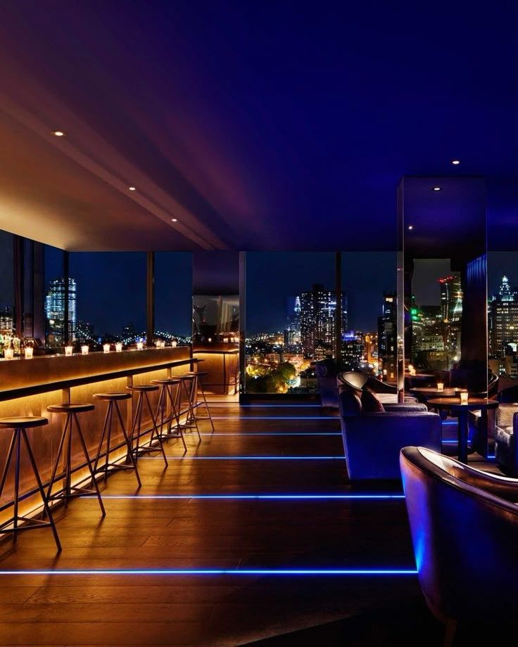 the bar is lit up at night with blue lights in the room and tall buildings behind it