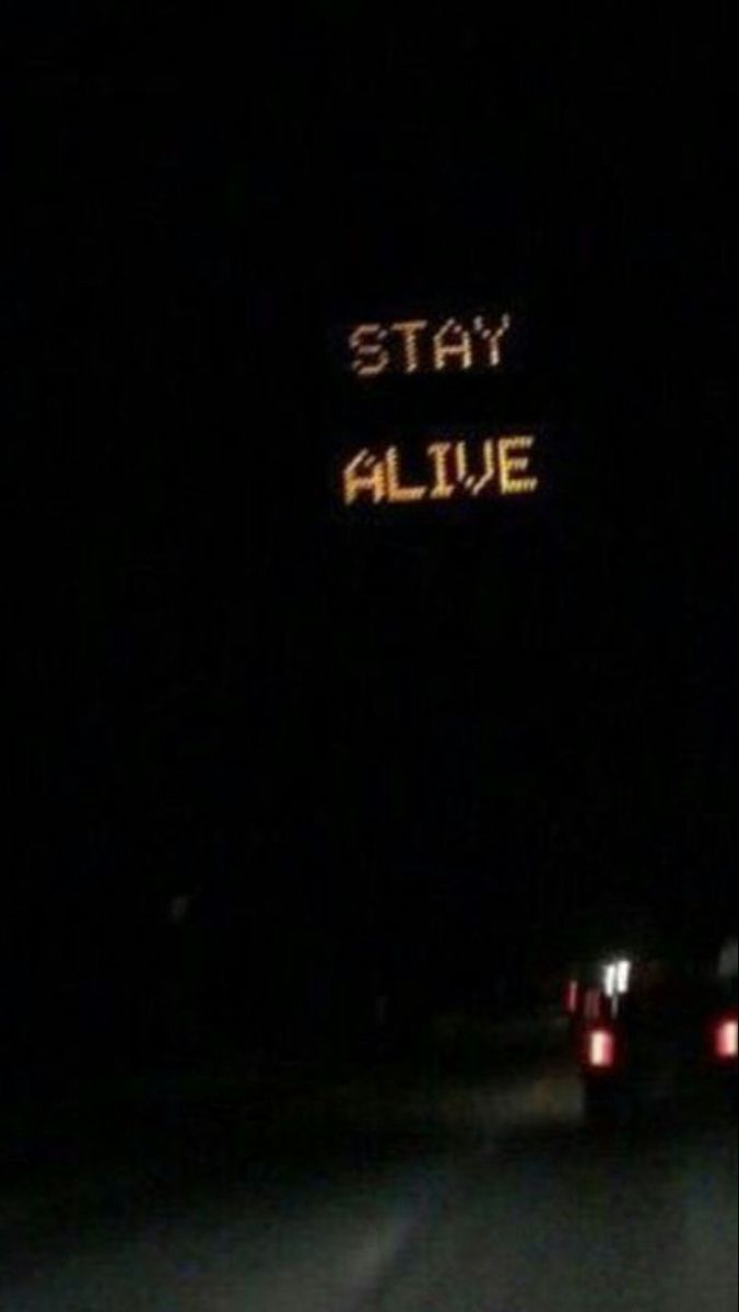 two cars driving down the road at night with an illuminated sign that says stay alive